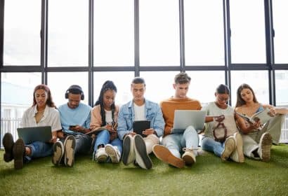 siete jovenes sentados juegan con ordenadores, teléfonos y tablet